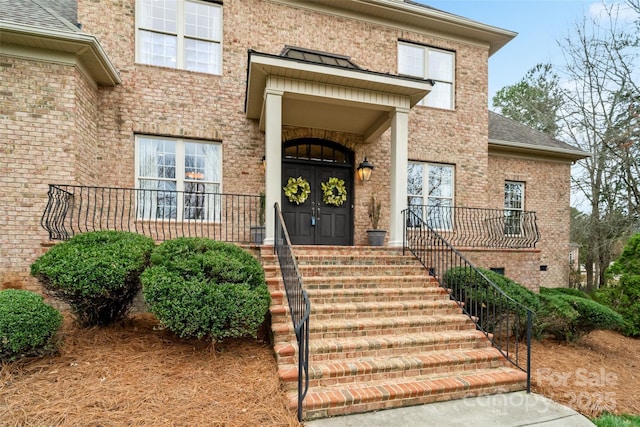 entrance to property featuring brick siding and roof with shingles