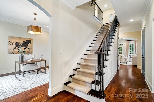 staircase with arched walkways, crown molding, and wood finished floors