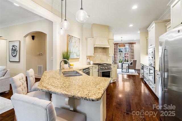 kitchen featuring dark wood finished floors, a peninsula, arched walkways, a sink, and stainless steel appliances