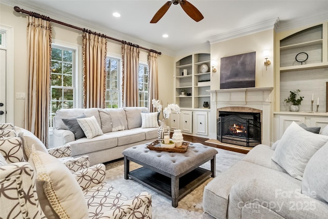 living area with crown molding, built in features, a lit fireplace, recessed lighting, and wood finished floors