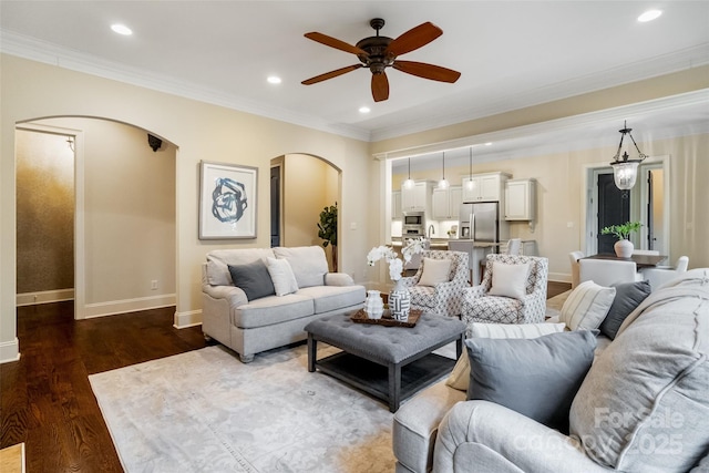 living area with dark wood-type flooring, baseboards, ornamental molding, recessed lighting, and arched walkways