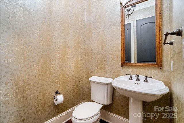 half bathroom featuring baseboards, toilet, and wallpapered walls