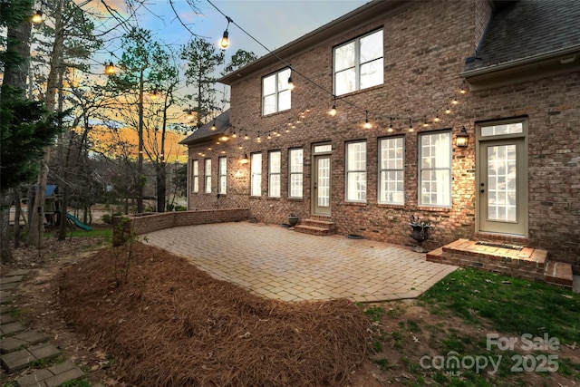 back of property featuring entry steps, a patio, a playground, roof with shingles, and brick siding