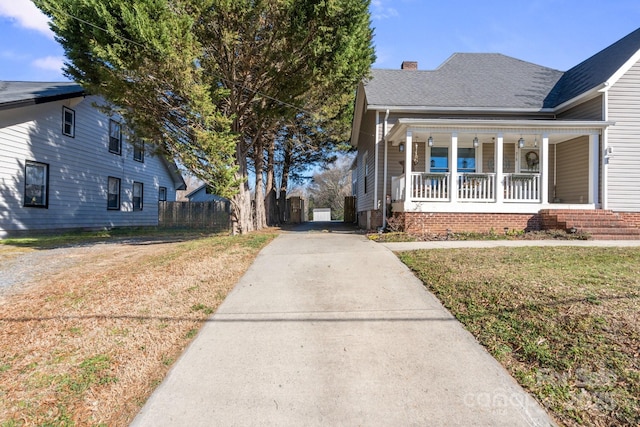 view of front facade with a chimney, covered porch, fence, driveway, and a front lawn