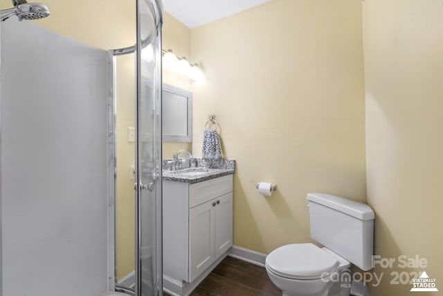full bathroom featuring toilet, wood finished floors, vanity, baseboards, and a stall shower