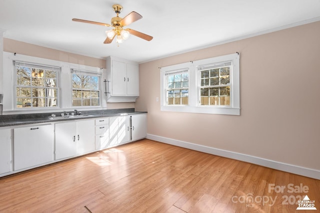 kitchen featuring light wood finished floors, dark countertops, a sink, and baseboards