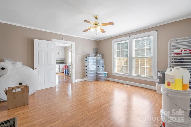 interior space with light wood finished floors, baseboards, ornamental molding, and a ceiling fan