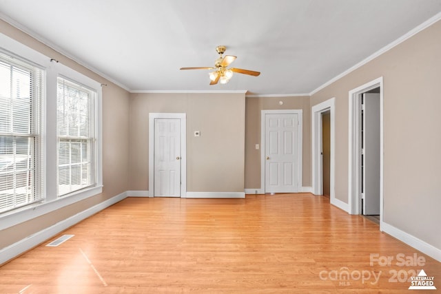 spare room with light wood finished floors, baseboards, visible vents, a ceiling fan, and ornamental molding