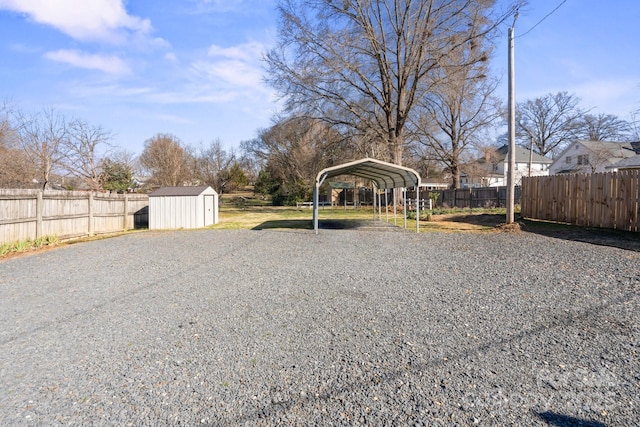 view of yard with gravel driveway, a detached carport, fence, a shed, and an outdoor structure