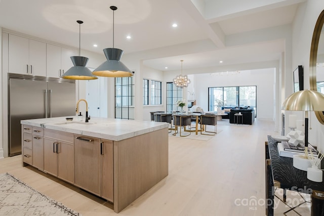 kitchen with light stone counters, a kitchen island with sink, a sink, and light wood finished floors