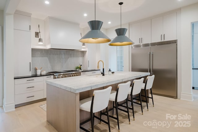 kitchen with built in refrigerator, a sink, light wood-style floors, exhaust hood, and stove