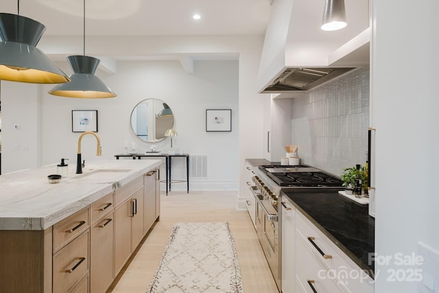 kitchen featuring visible vents, light wood finished floors, a sink, custom range hood, and tasteful backsplash