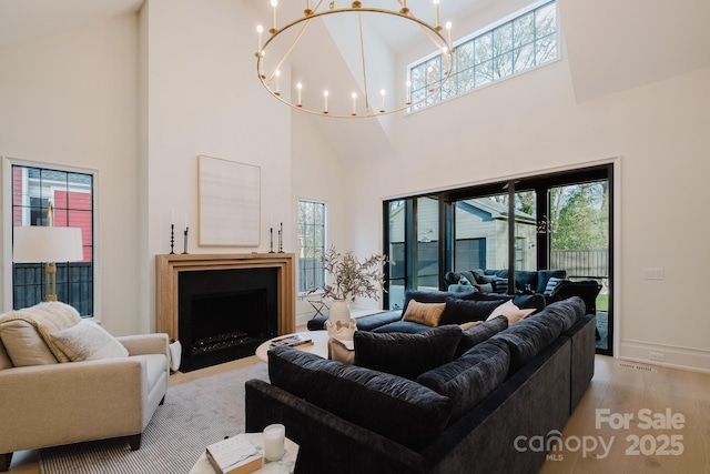 living area with baseboards, a fireplace with flush hearth, an inviting chandelier, light wood-style floors, and a towering ceiling