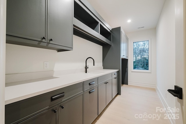 kitchen featuring visible vents, light countertops, baseboards, and a sink