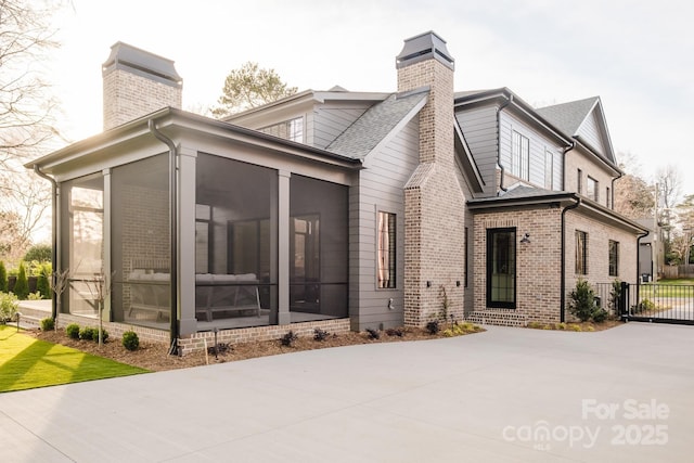 view of side of home featuring brick siding, a shingled roof, a chimney, a sunroom, and driveway