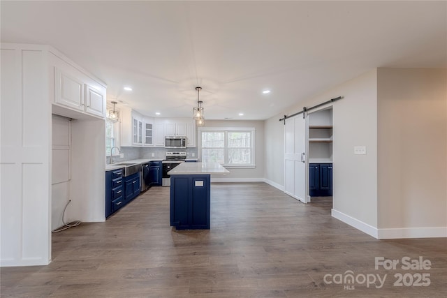 kitchen with blue cabinetry, a sink, white cabinetry, a barn door, and appliances with stainless steel finishes