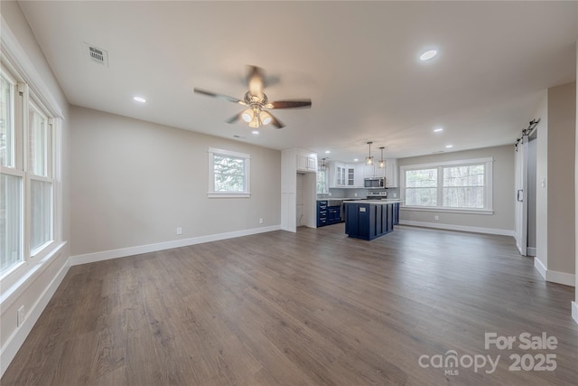 unfurnished living room with dark wood finished floors, a barn door, a ceiling fan, and visible vents