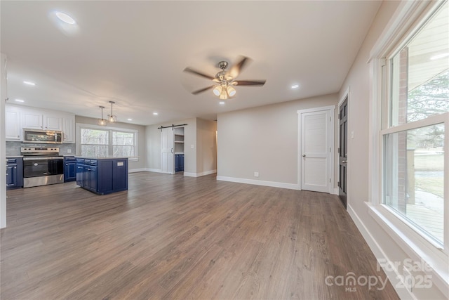 kitchen featuring ceiling fan, a barn door, wood finished floors, stainless steel appliances, and blue cabinets