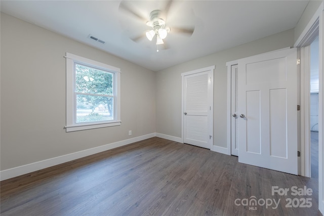 unfurnished bedroom with visible vents, two closets, a ceiling fan, dark wood-style floors, and baseboards