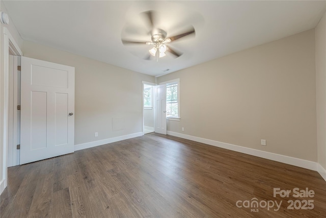 empty room with baseboards, ceiling fan, and dark wood-style flooring