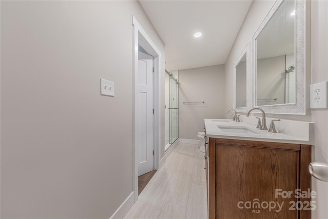 full bath with baseboards, double vanity, a sink, toilet, and a shower with door