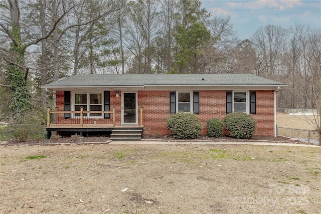 single story home featuring brick siding, covered porch, roof with shingles, and fence