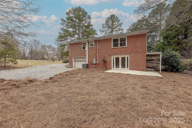 back of house with brick siding, gravel driveway, fence, french doors, and an attached garage