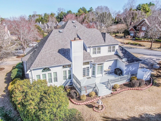 back of house featuring a chimney, concrete driveway, and a shingled roof