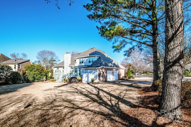 rear view of house featuring a garage, driveway, and a chimney