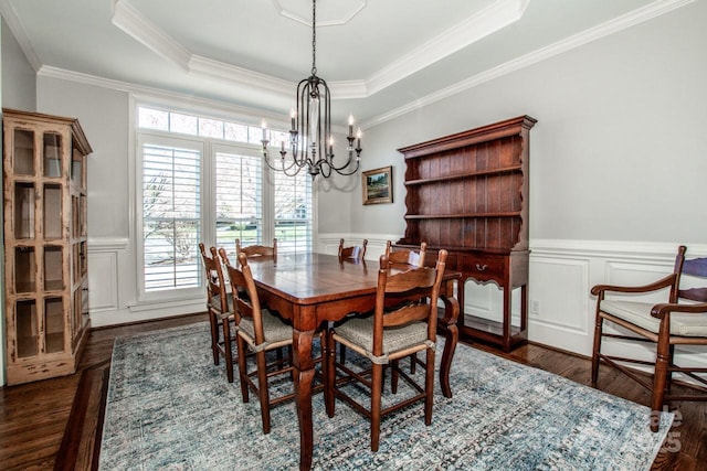 dining space featuring a wainscoted wall, a raised ceiling, dark wood-type flooring, and an inviting chandelier