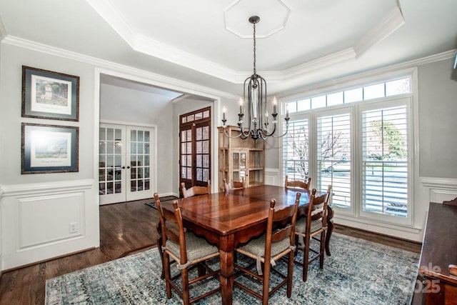 dining area featuring a decorative wall, french doors, a raised ceiling, and wood finished floors