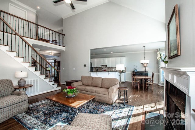 living area featuring visible vents, high vaulted ceiling, dark wood-type flooring, stairway, and crown molding