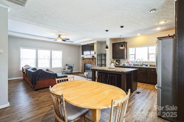 dining area featuring a brick fireplace, baseboards, visible vents, and wood finished floors