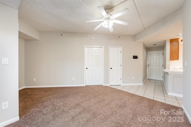 spare room featuring light tile patterned flooring, light colored carpet, baseboards, and ceiling fan