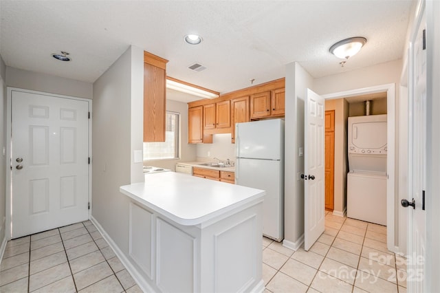 kitchen featuring stacked washer / drying machine, visible vents, light tile patterned flooring, and freestanding refrigerator