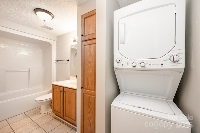 laundry area featuring stacked washer / dryer, visible vents, laundry area, light tile patterned flooring, and a textured ceiling