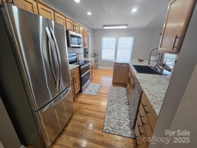 kitchen featuring light wood-style flooring, recessed lighting, a sink, decorative backsplash, and appliances with stainless steel finishes