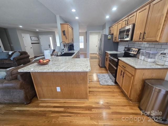 kitchen featuring a peninsula, a sink, appliances with stainless steel finishes, open floor plan, and backsplash