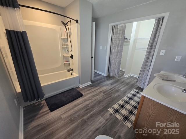 full bathroom featuring shower / bathtub combination with curtain, wood finished floors, baseboards, double vanity, and a sink