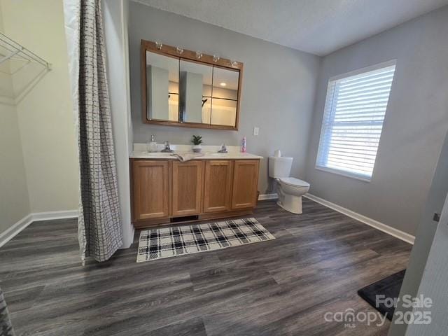 bathroom with double vanity, toilet, wood finished floors, and baseboards