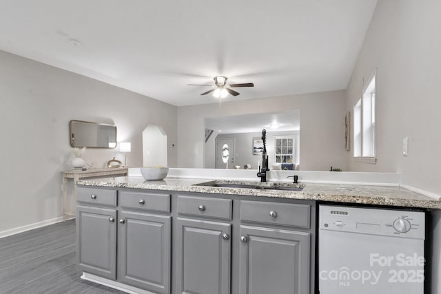 kitchen featuring light stone counters, gray cabinetry, a ceiling fan, a sink, and white dishwasher