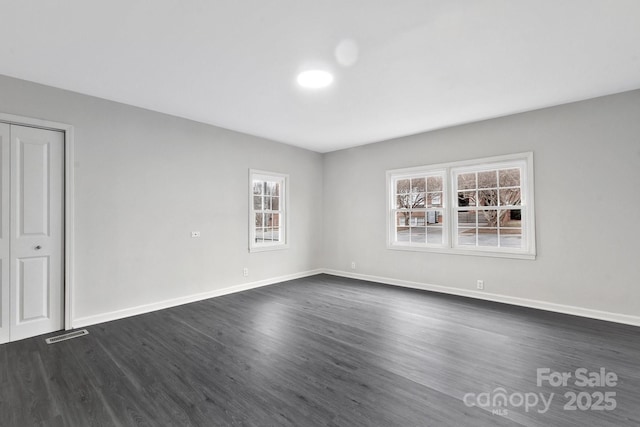 spare room with dark wood-style floors, visible vents, and baseboards