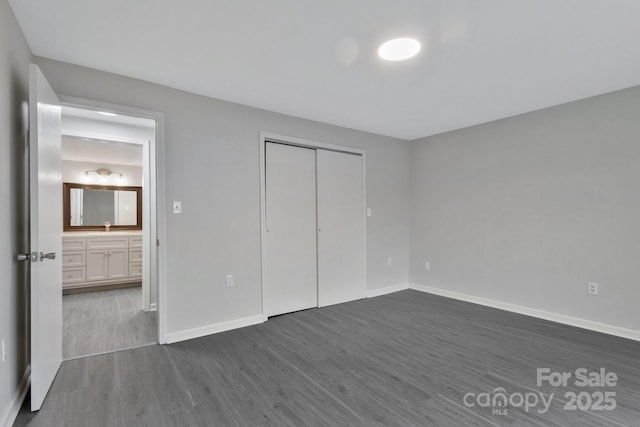 unfurnished bedroom featuring a closet, baseboards, dark wood finished floors, and a sink