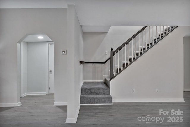 stairs featuring arched walkways, wood finished floors, and baseboards