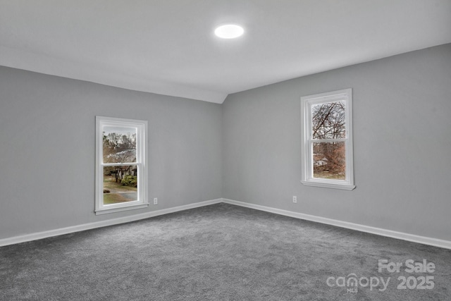 unfurnished room featuring baseboards, dark carpet, and a healthy amount of sunlight