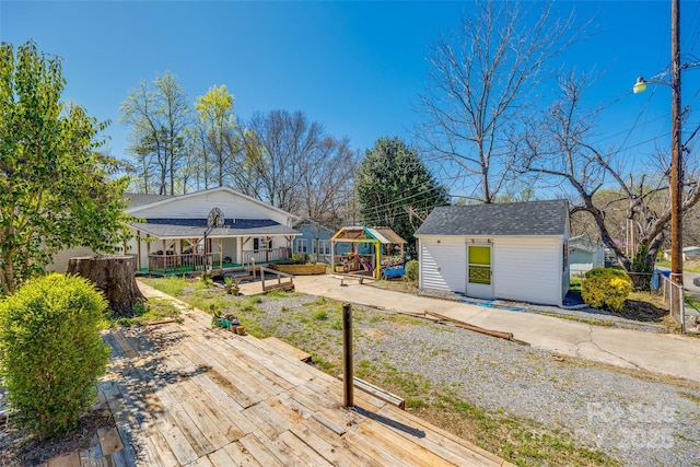 back of house with an outbuilding, roof with shingles, fence, a garden, and a wooden deck