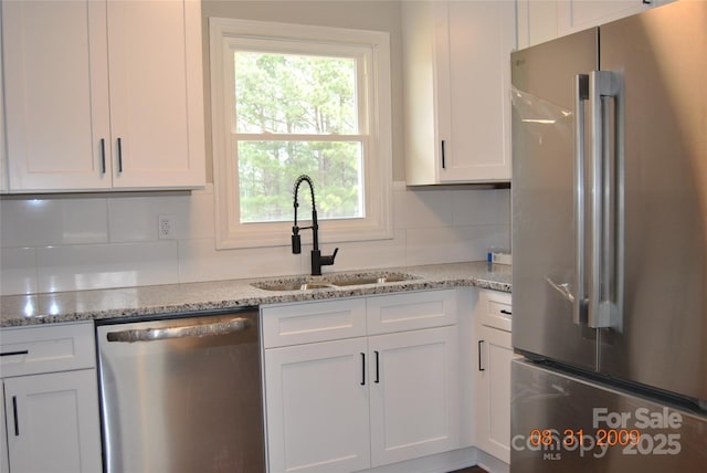 kitchen featuring a sink, tasteful backsplash, appliances with stainless steel finishes, white cabinets, and light stone countertops