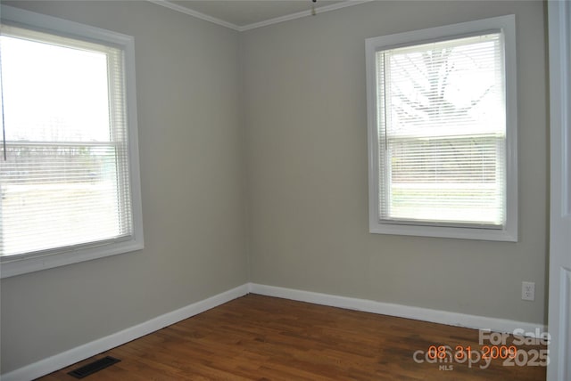 spare room featuring visible vents, baseboards, ornamental molding, and dark wood-style flooring