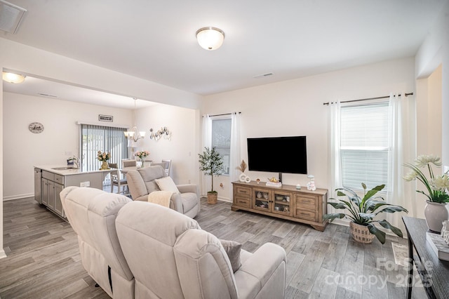 living area with a notable chandelier, baseboards, visible vents, and light wood-type flooring