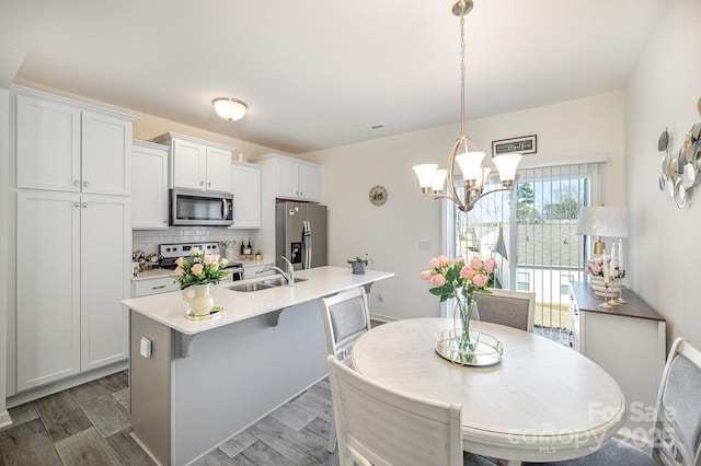 kitchen with a sink, an island with sink, decorative backsplash, appliances with stainless steel finishes, and dark wood-style flooring